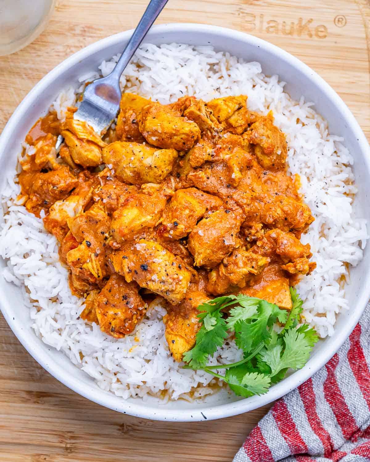 A white bowl of butter chicken over basmati rice.