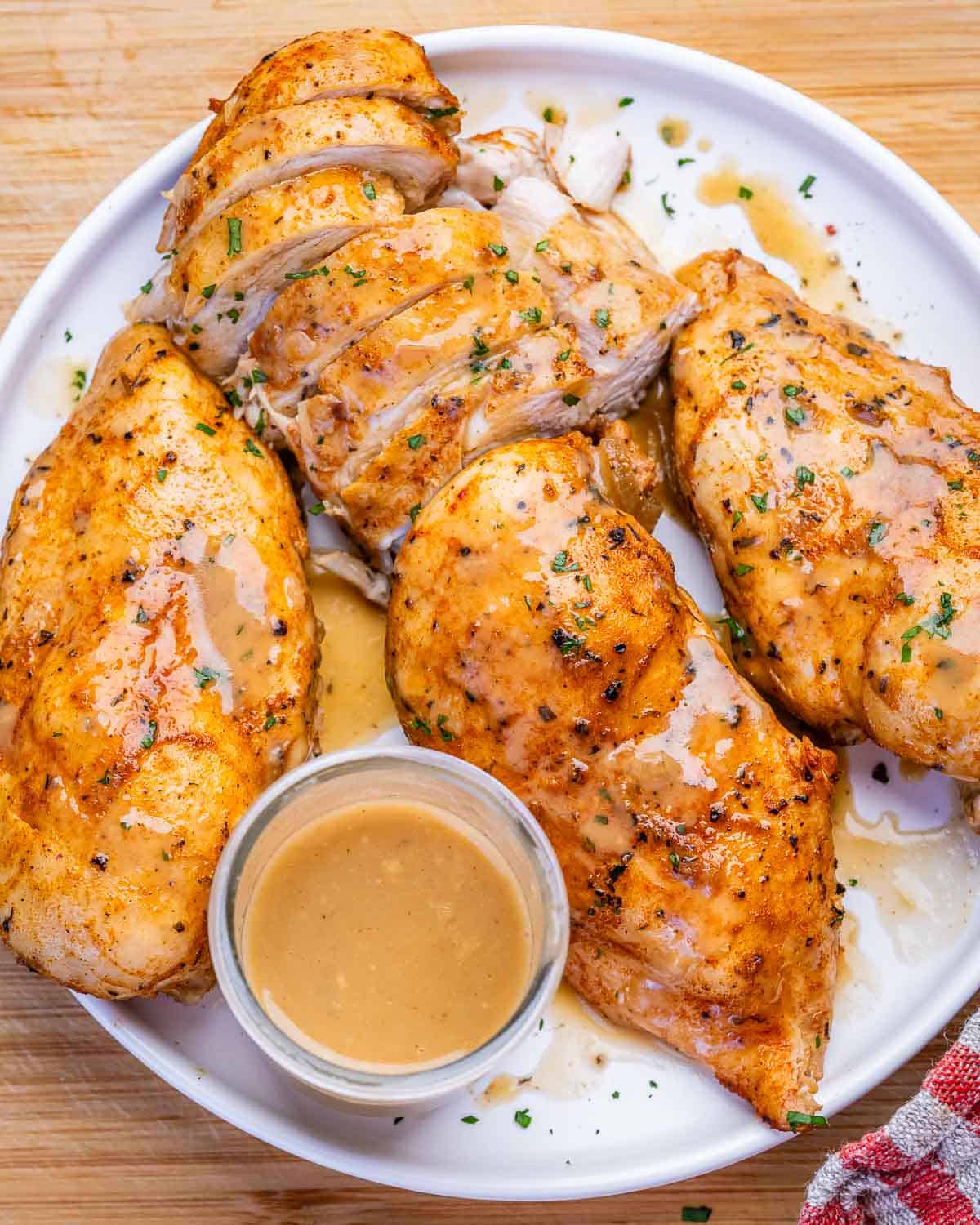 A white plate of instant pot chicken breasts with a jug of onion gravy.