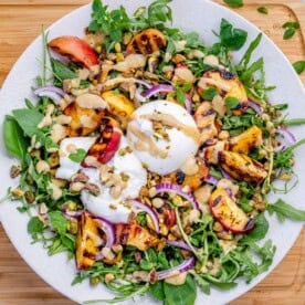 a plate with arugula salad topped with burrata and grilled peach.
