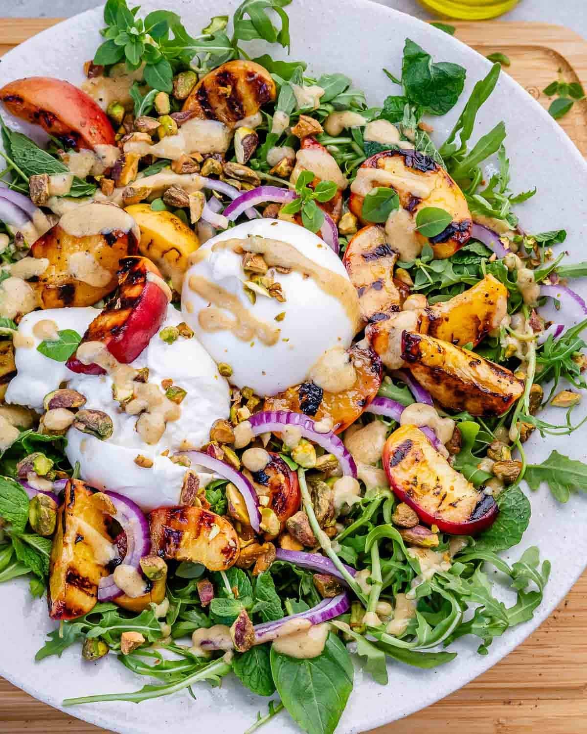 A peach burrata salad with arugula on a white plate.