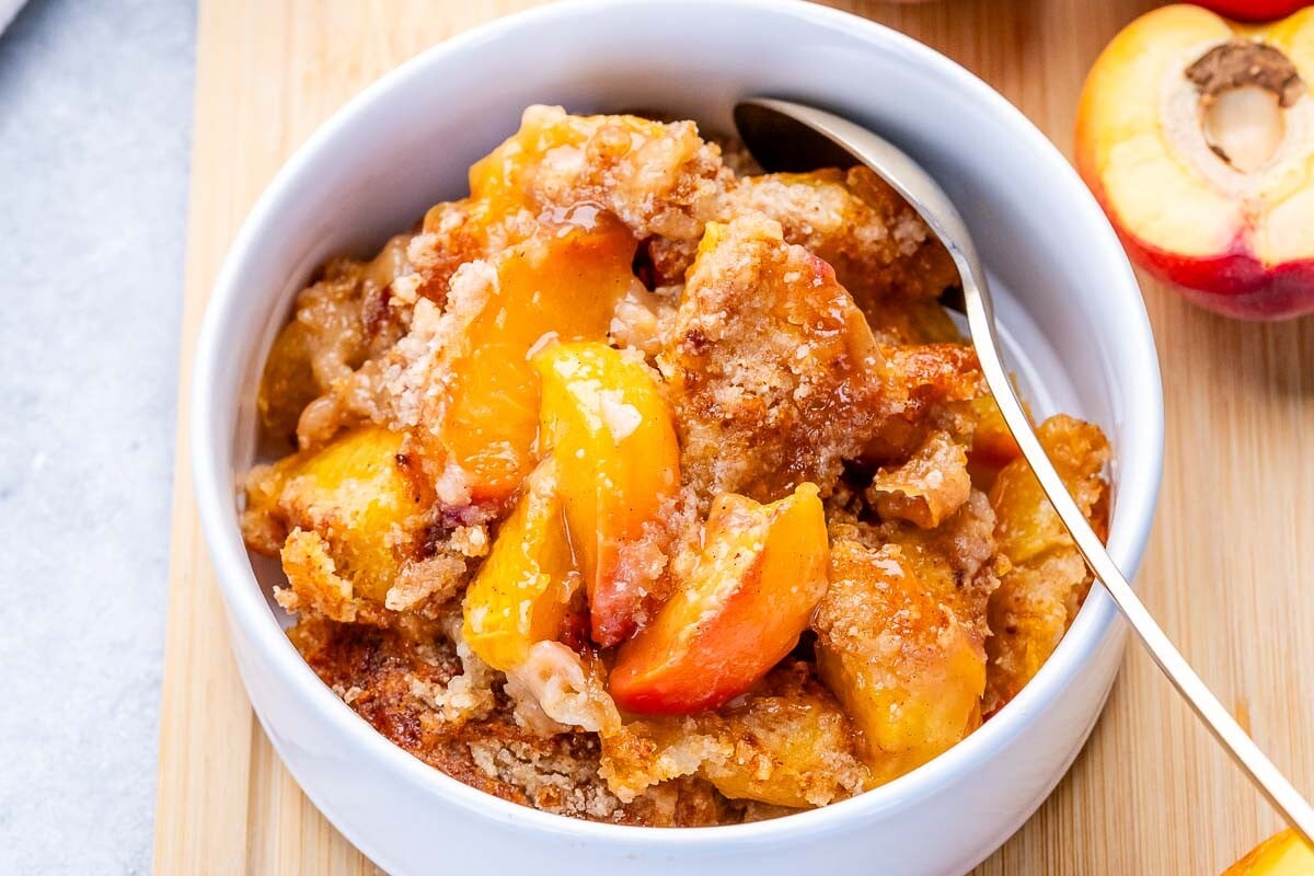 peach dump cake in a round white bowl with a spoon in it.