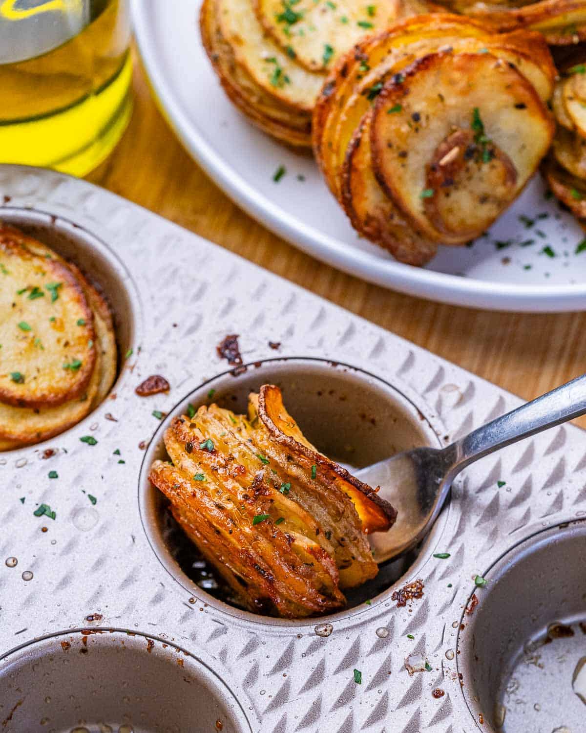 Crispy potato stacks in a muffin pan being scooped out with a spoon.