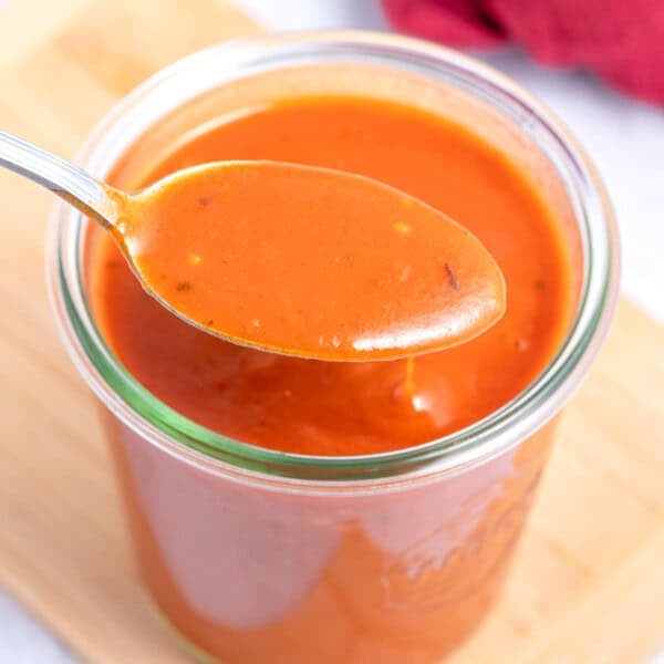 a jar filled with red enchilada sauce with a spoonful over the jar.