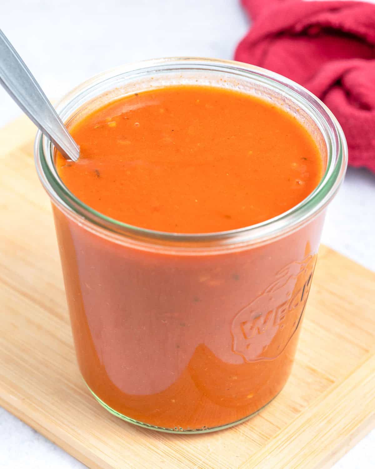 a jar with red enchilada sauce with a spoon in the jar.
