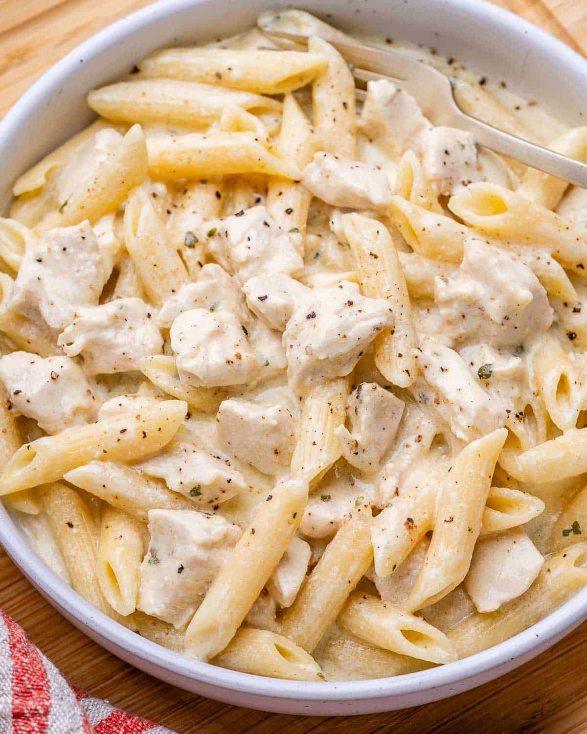 Slow cooker chicken alfredo with penne pasta in a white bowl.