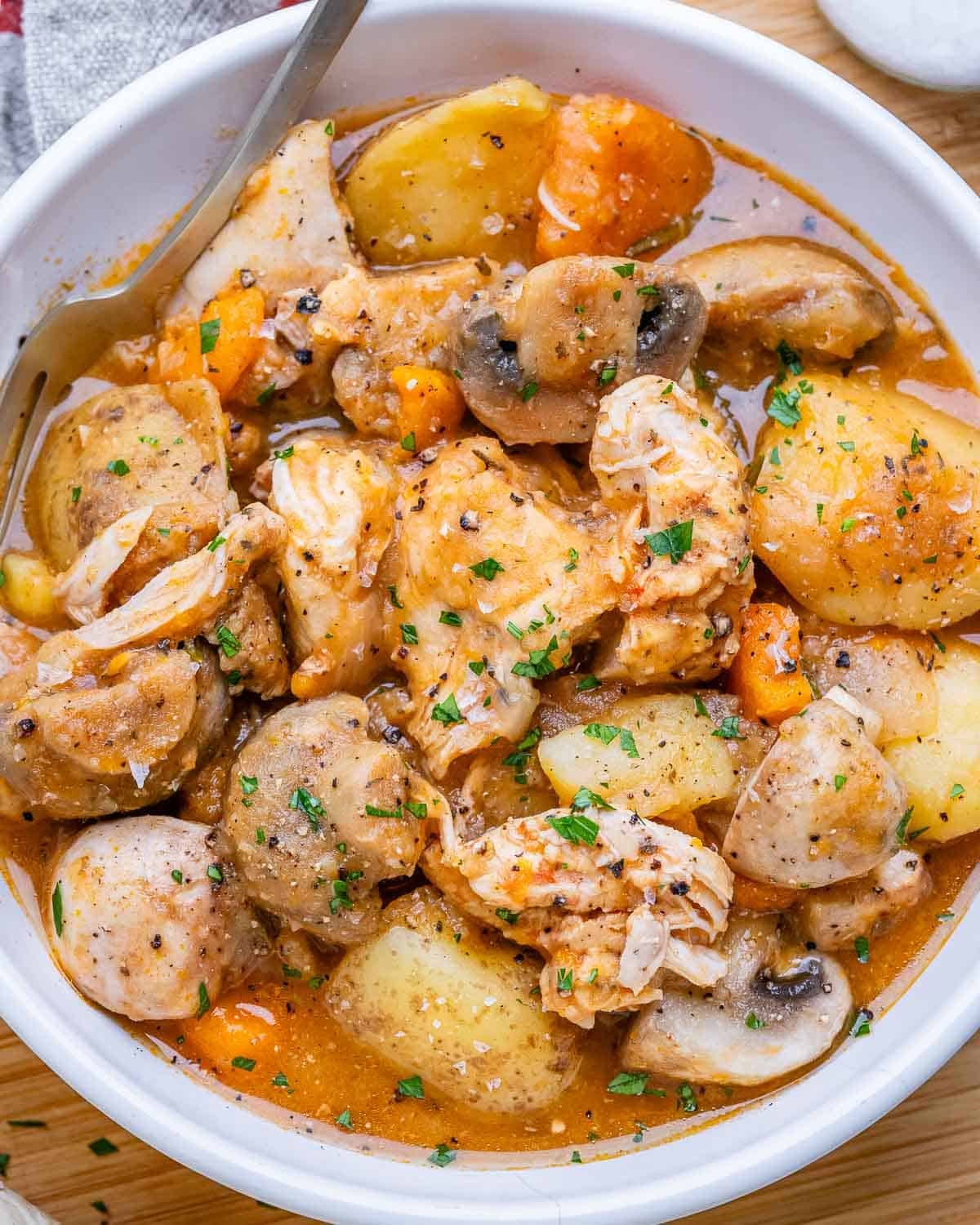 A white bowl of slow cooker chicken stew with potatoes and mushrooms.