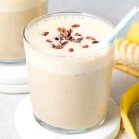 a glass with banana protein shake topped with cocoa nibs.