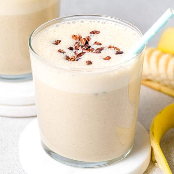 a glass with banana protein shake topped with cocoa nibs.