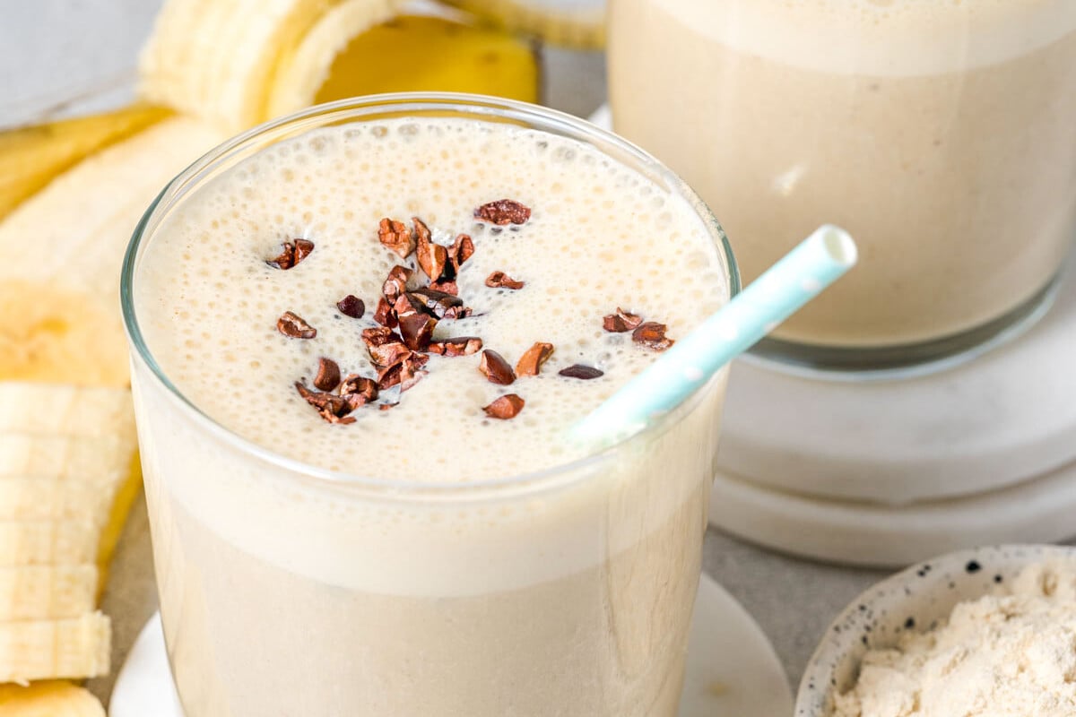 protein shake in a jar topped with cocoa nibs and has a straw in it.