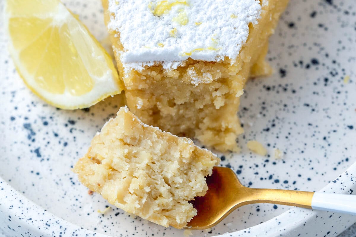 a bite taken off the lemon cake with a fork on a plate.