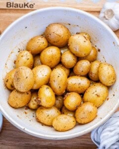 baby potatoes tossed in a bowl with oil and seasoning.