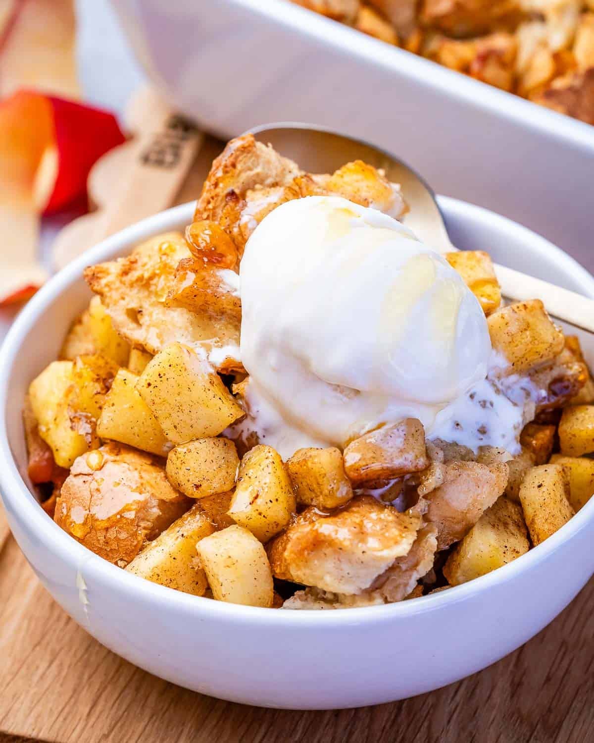 A white bowl filled with apple bread pudding topped with a scoop of ice cream.