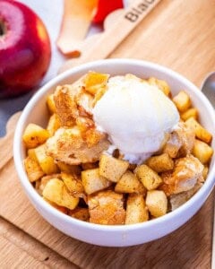 A white bowl of apple bread pudding topped with vanilla ice cream.