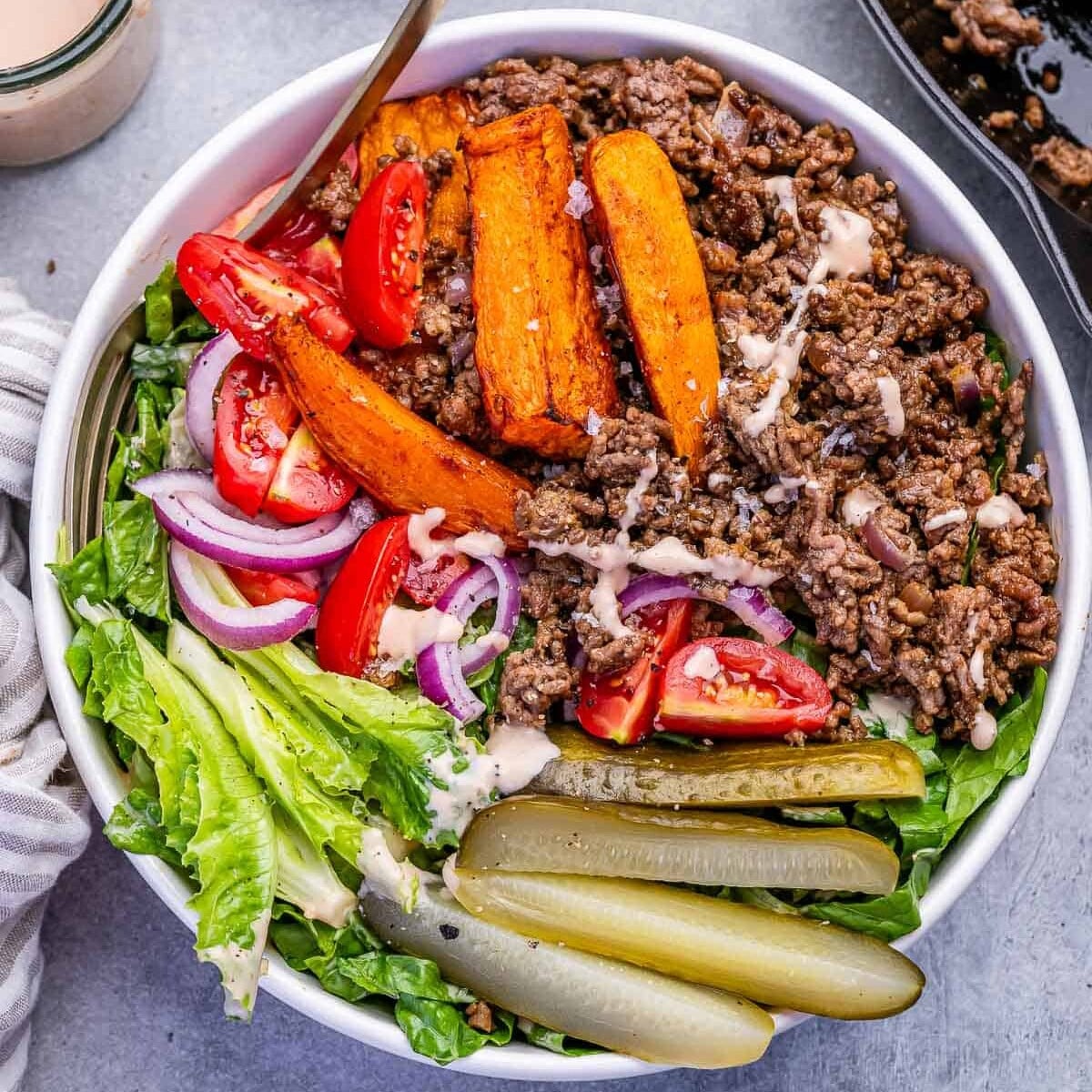 a bowl filled with lettuce, topped with seasoned beef and burger topping ingredients.
