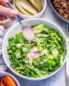 adding dressing over chopped romaine lettuce.
