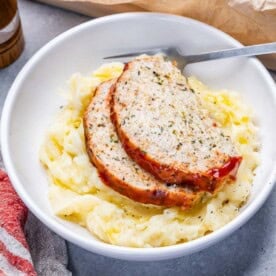 a serving of mashed potatoes topped with 2 slices of chicken meatloaf in a round bowl.