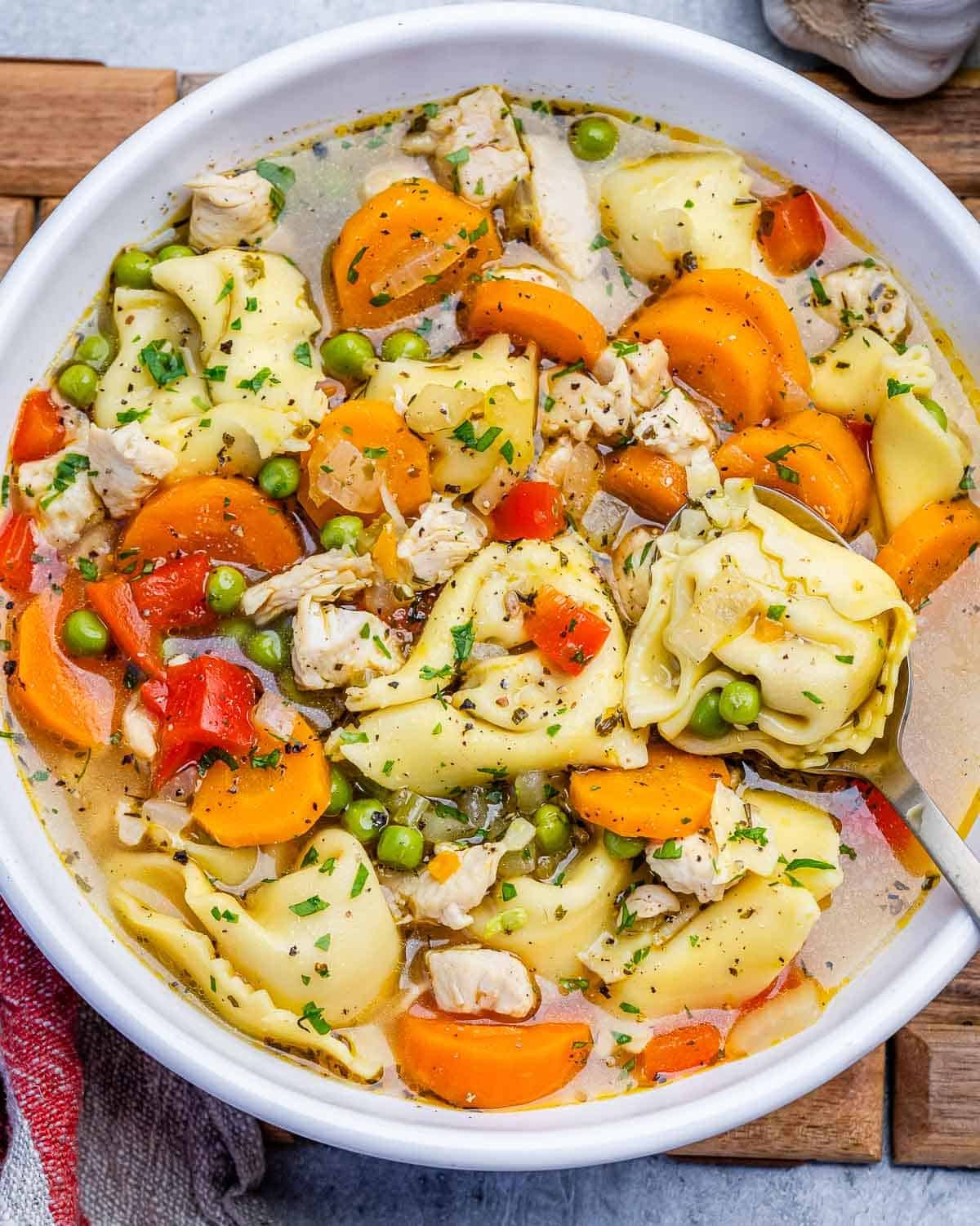a bowl filled with chicken tortellini soup with carrots and peas.