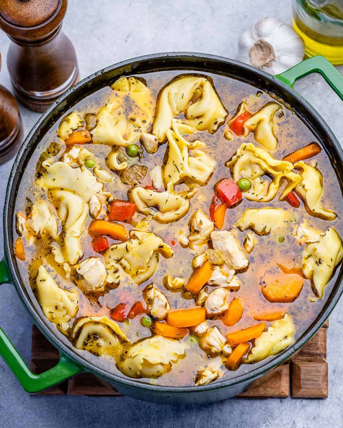 A green pot filled with chicken tortellini soup.
