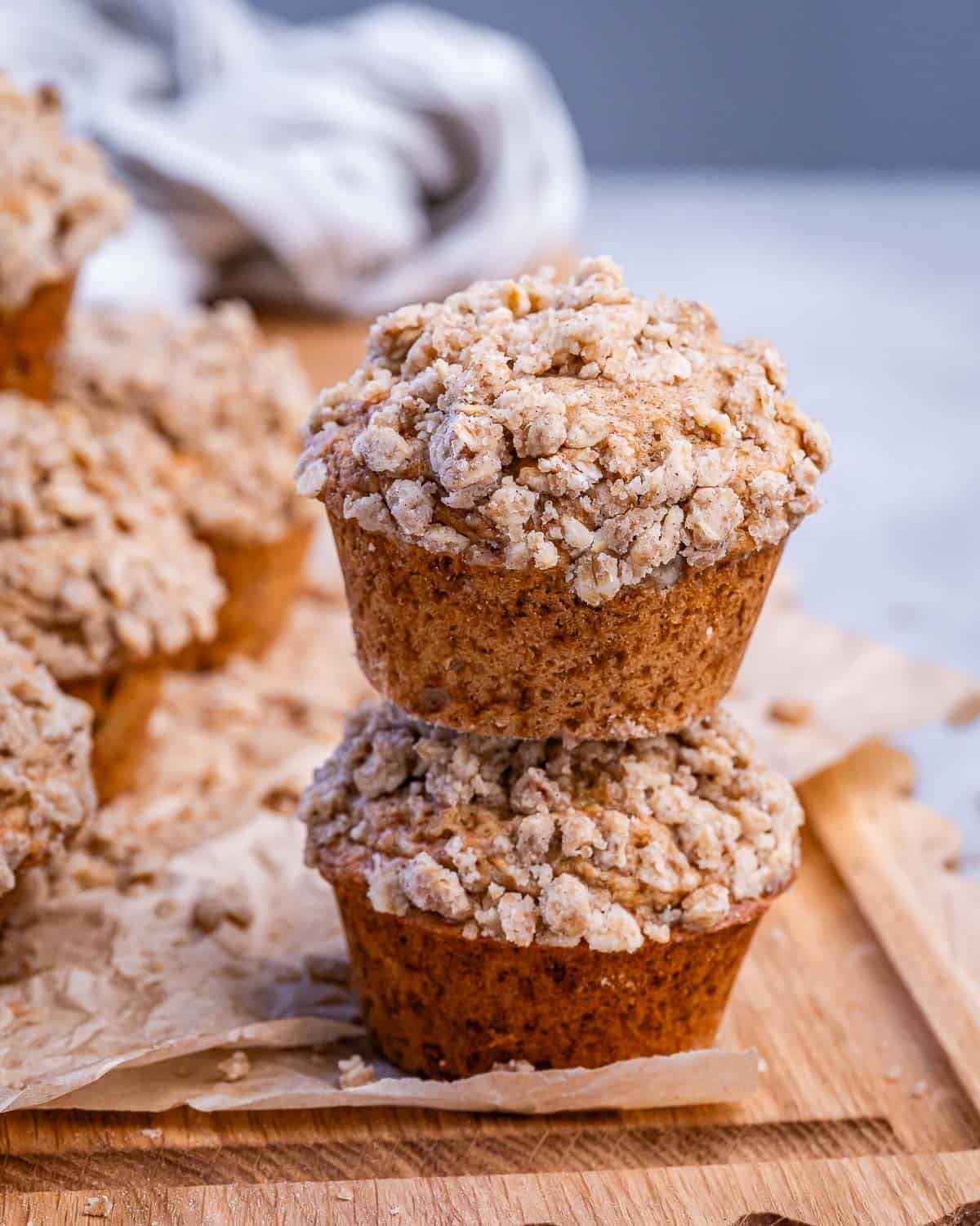 Two cinnamon streusel muffins stacked on a wooden board.