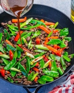 pouring sauce over the beef and veggies for the stir fry in a pan.