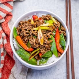 a bowl filled with rice topped with ground beef stir fry , snap peas, and red peppers.