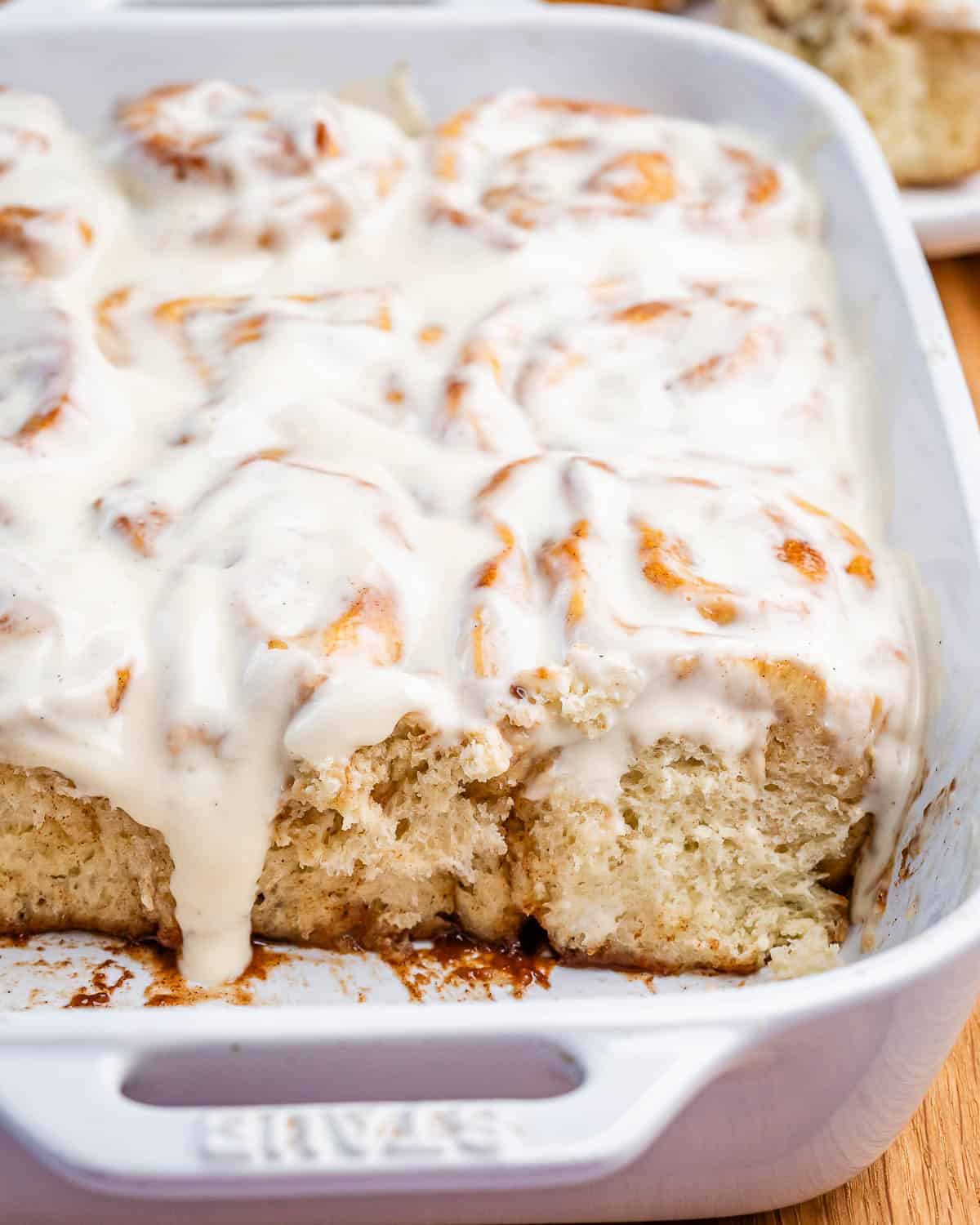 Homemade cinnamon rolls with cream cheese glaze in a white baking dish.