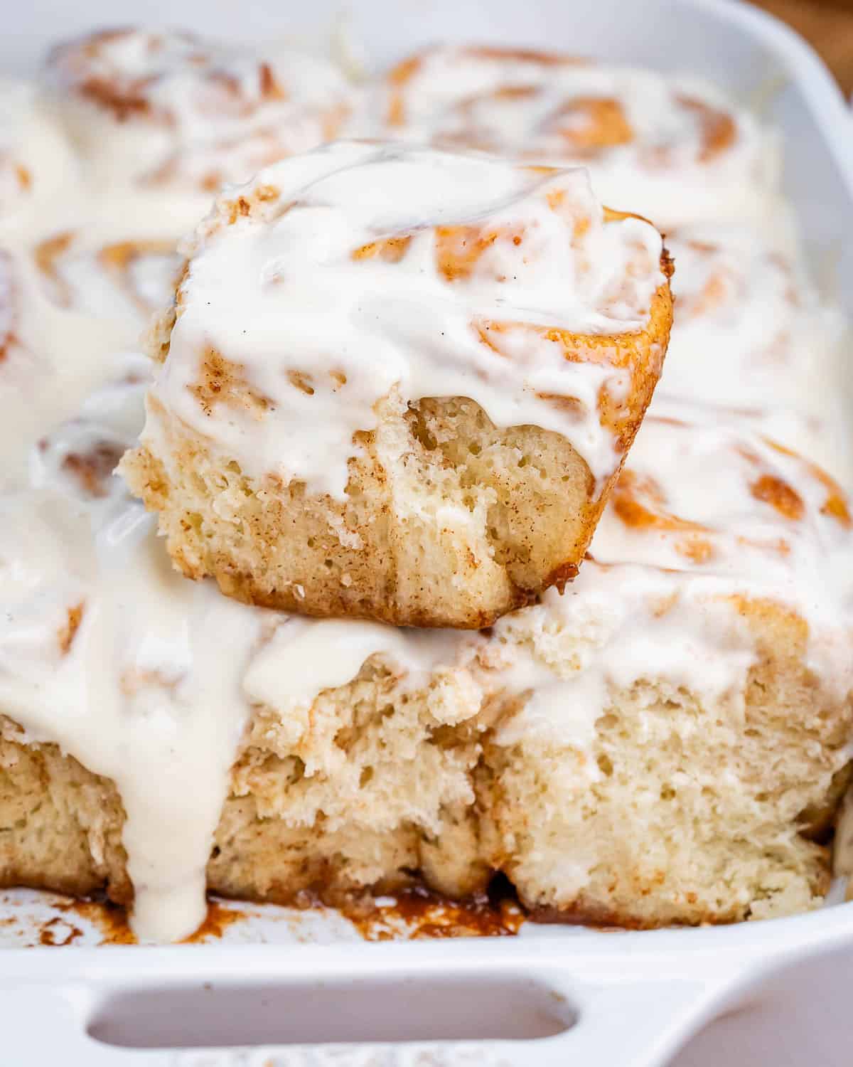 A white dish with cinnamon rolls, with one roll stacked on top.