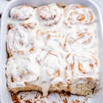 cinnamon rolls in cream cheese frosting in a baking dish.