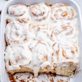 cinnamon rolls in cream cheese frosting in a baking dish.