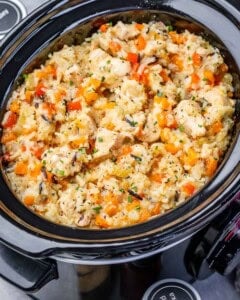 A slow cooker filled with chicken, wild rice and diced vegetables.