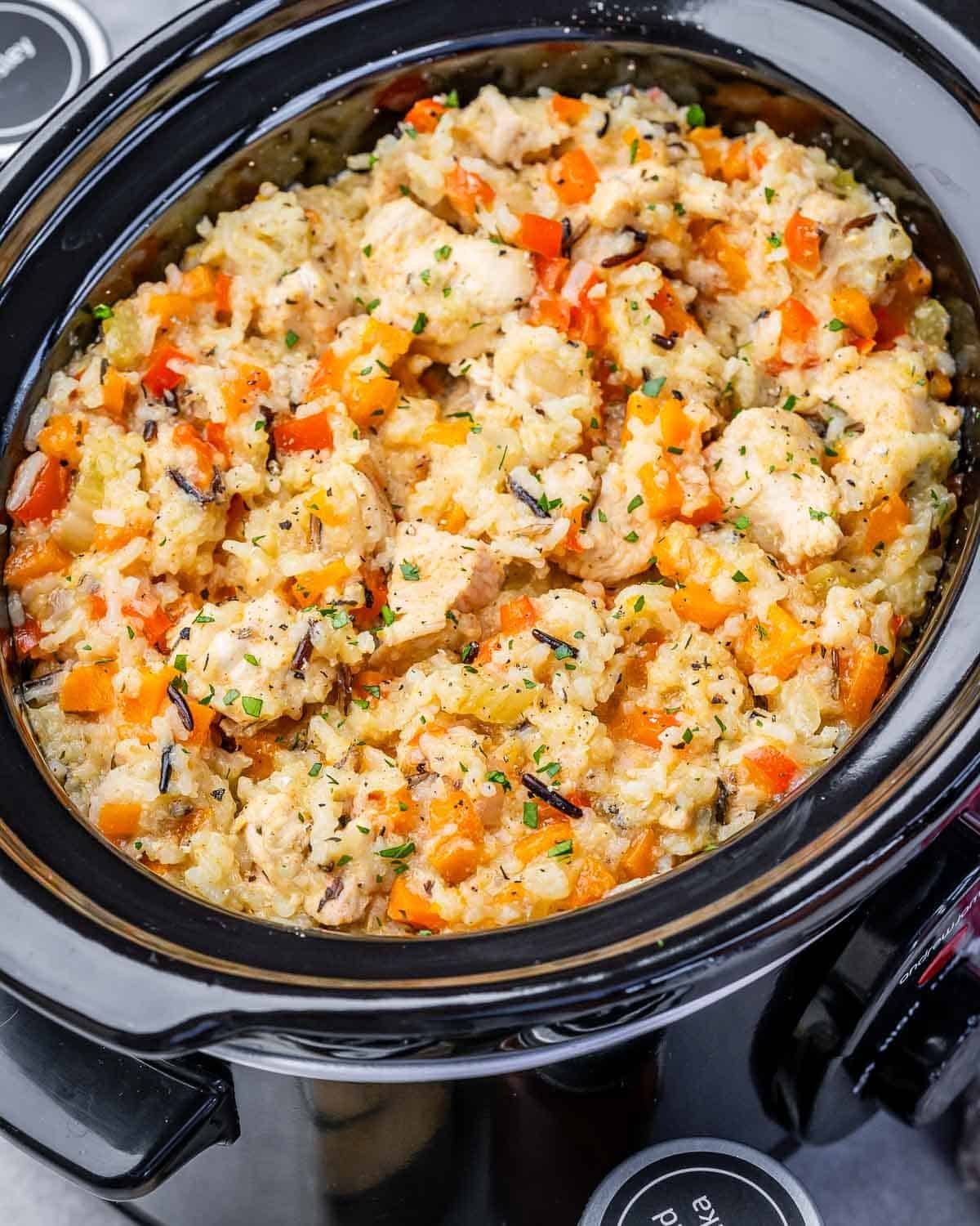 A slow cooker filled with chicken, wild rice and diced vegetables.