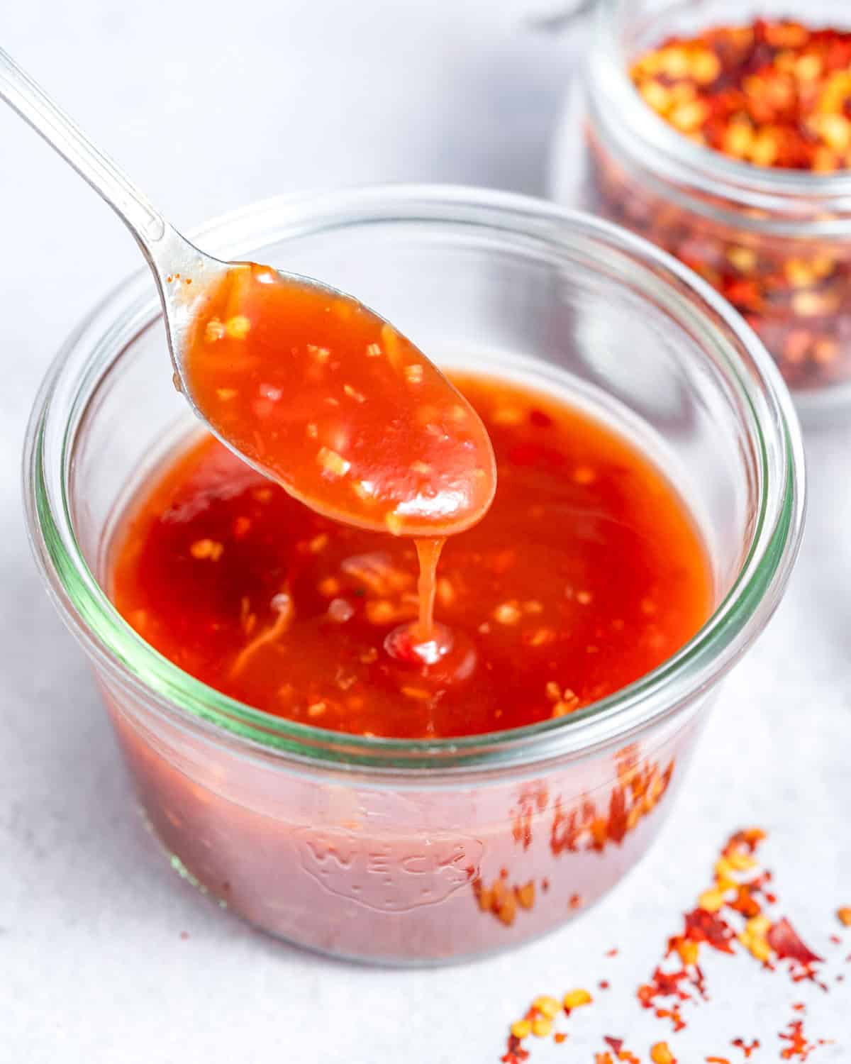 A jar of sweet chili sauce with a spoon drizzling it back into the jar.