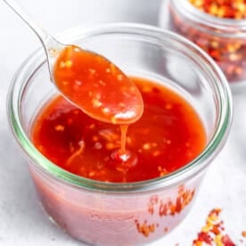 a jar with sweet chili sauce with a spoonful digging into the bowl.