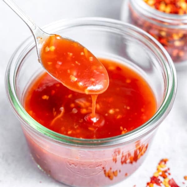 a jar with sweet chili sauce with a spoonful digging into the bowl.