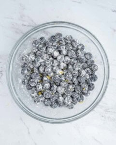 blueberries tossed with four and lemon zest in a bowl.