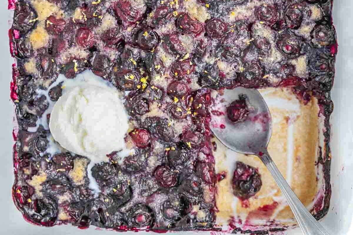 a dish with a portion of blueberry cobbler sliced off topped with ice cream portions.