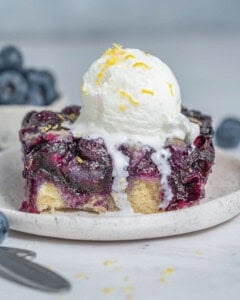 a slice of blueberry cobbler on a plate with a serving of icecream over it.