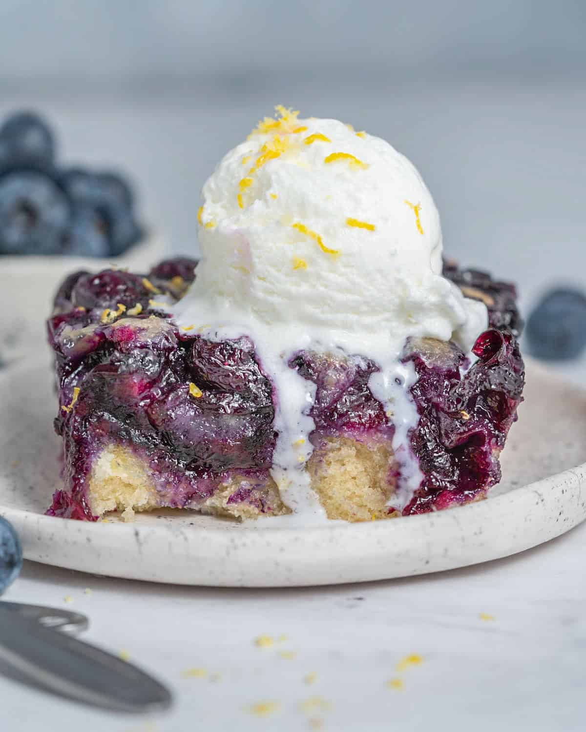 a slice of blueberry cobbler on a plate with a serving of icecream over it.