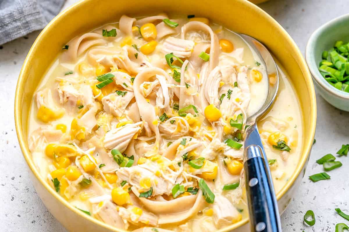 a yellow bowl with chicken corn soup and a spoon in the bowl.