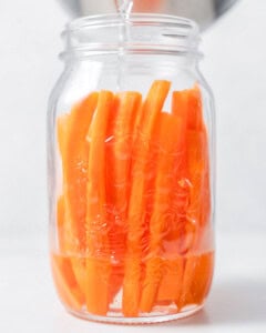 brine being poured into a jar with carrot sticks.