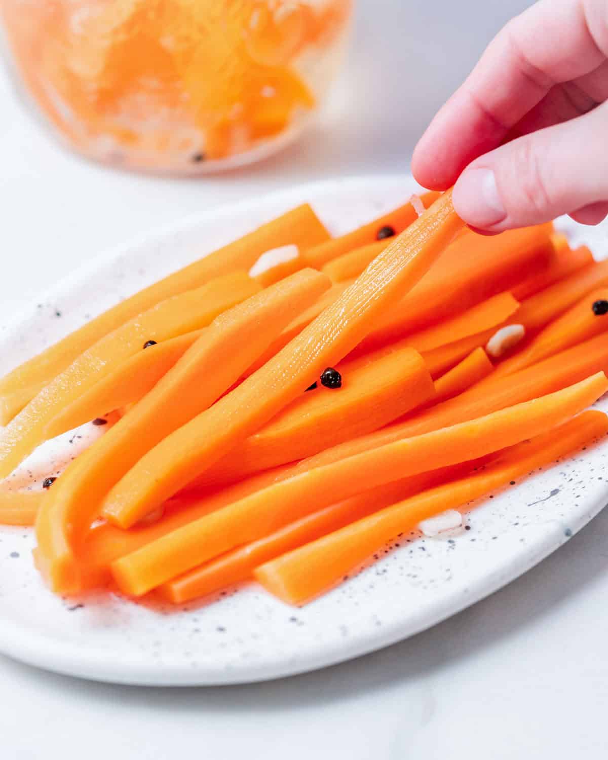 Hand grabbing a pickled carrot stick from a plate.