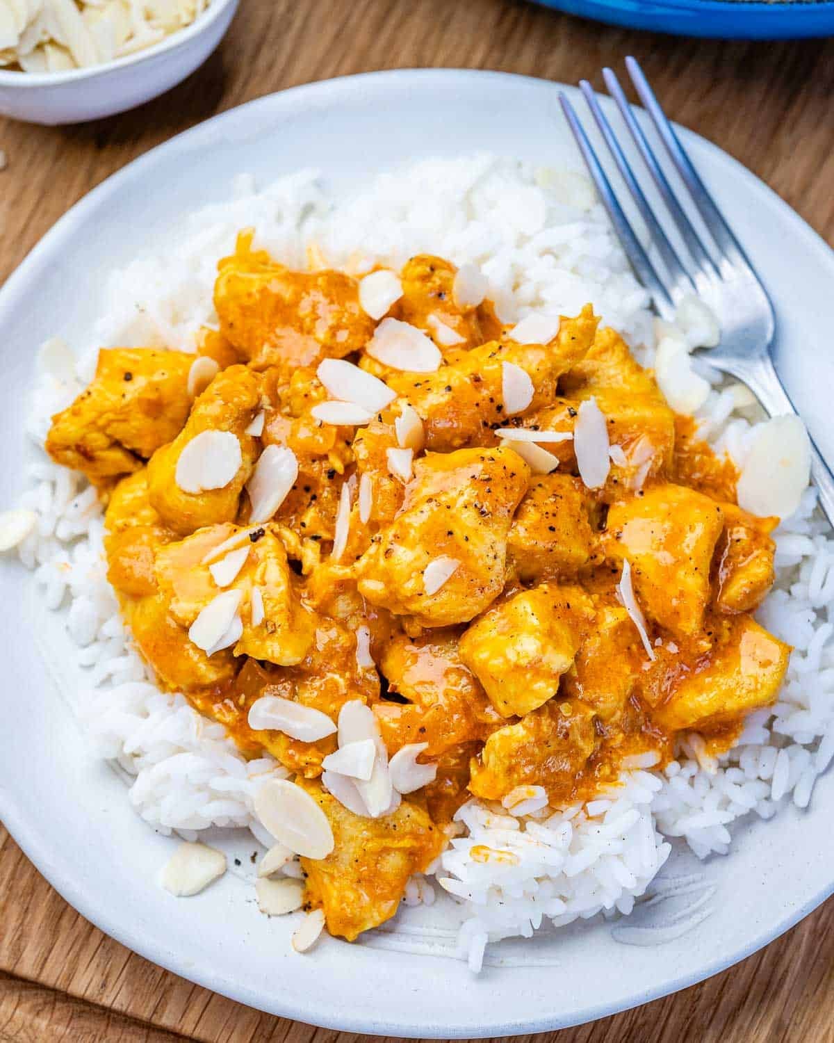 A white bowl with rice and chicken korma topped with flaked almonds.