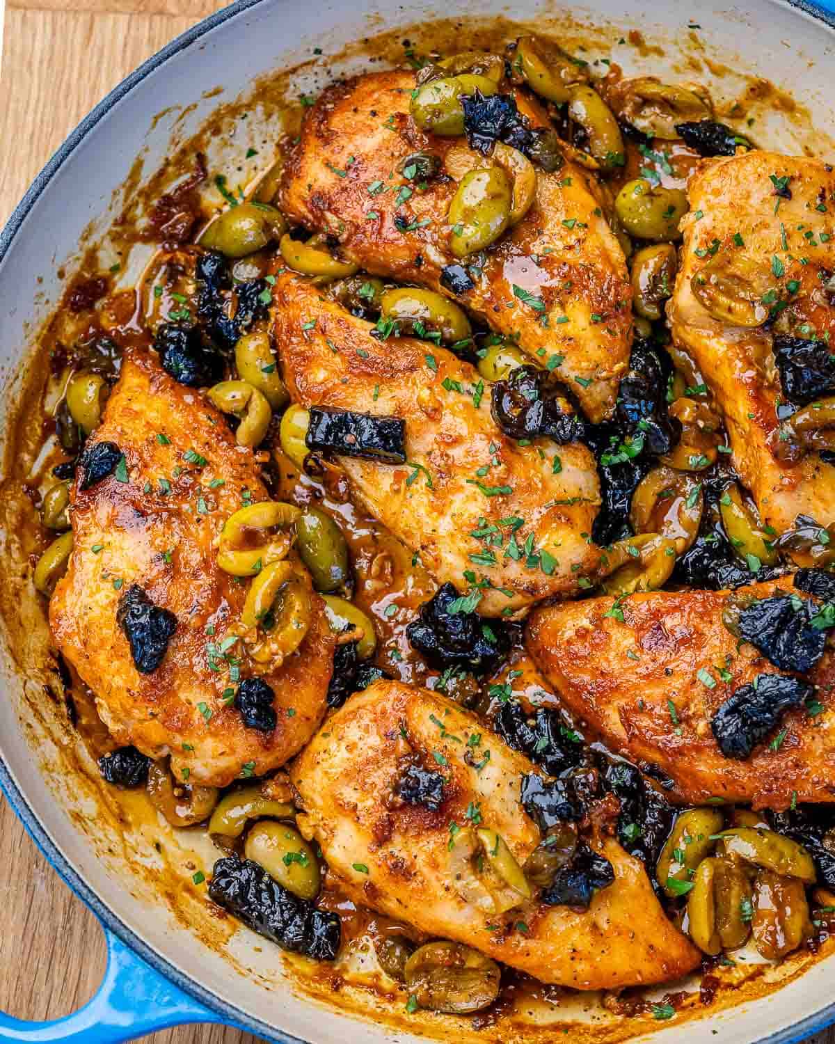 A blue skillet with chicken marbella, olives, prunes and parsley.