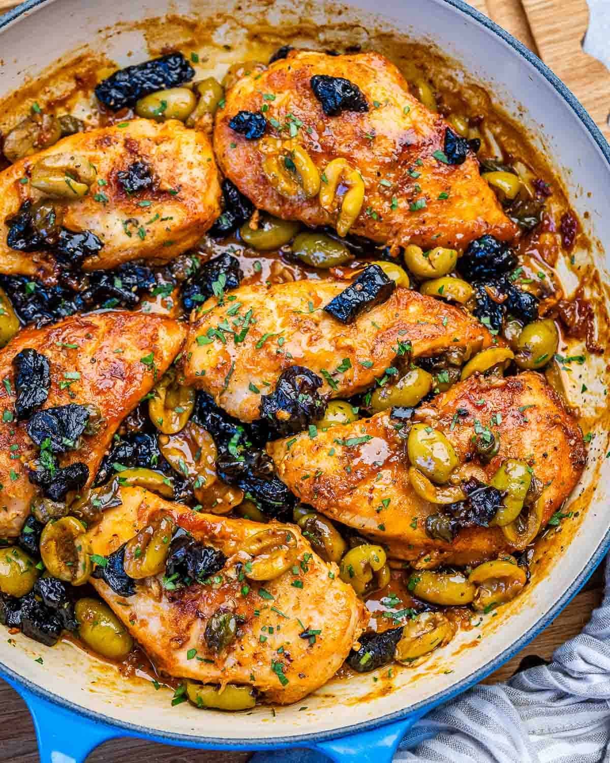 chicken in marbella sauce with prunes and olives in a skillet.