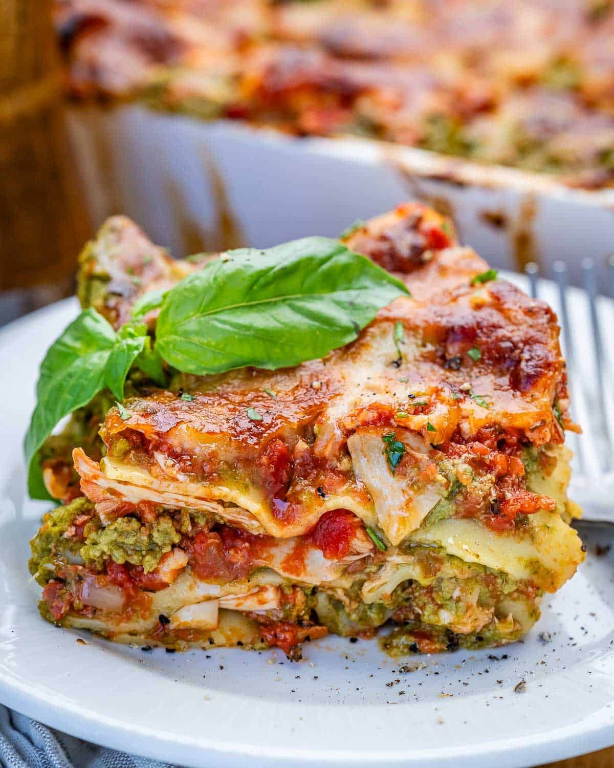 A slice of chicken lasagna on a white plate topped with basil.