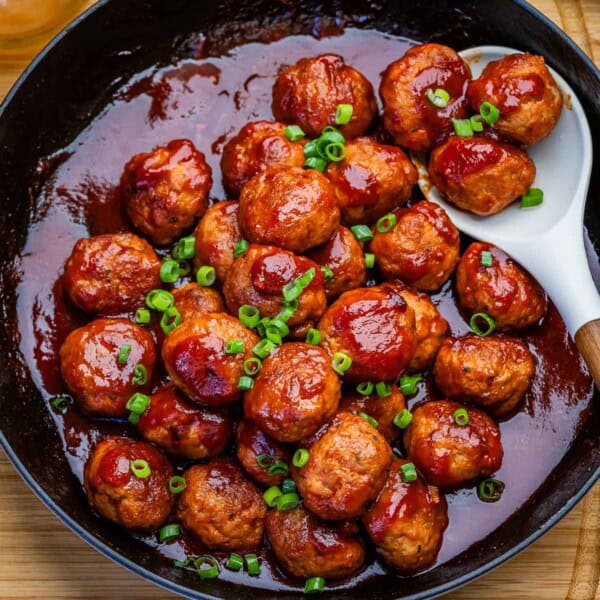 meatballs in a grape jelly tomato sauce in a skillet.