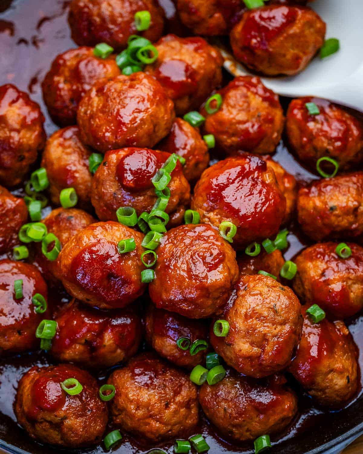Grape jelly meatballs in a skillet with a white spoon.