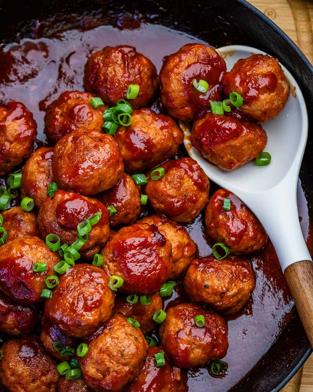 A skillet of grape jelly meatballs garnished with green onions.