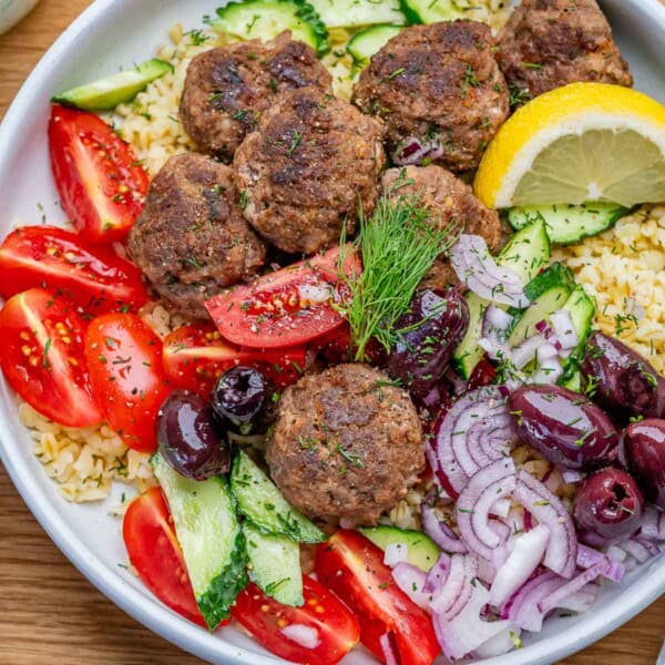 greek ground beef meatballs in a bowl with tomatoes over cooked bulgur.