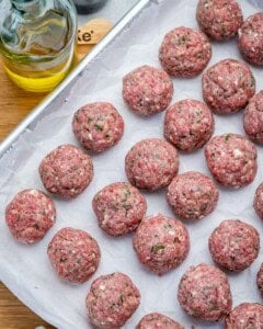 uncooked meatballs placed on a sheetpan.